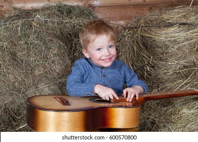 Little cheerful red-haired boy playing guitar in the hayloft - Powered by Shutterstock