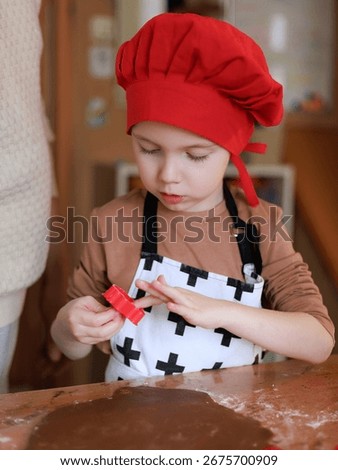 Little chef in red hat using cookie cutter for gingerbread dough before Christmas, holiday tradition at home. Copy space.