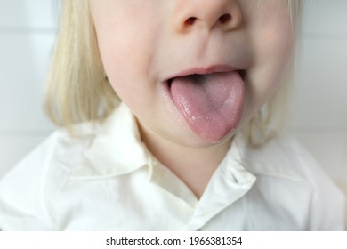 little child, baby, blonde girl showing tongue, mouth close-up, , concept of speech disorders, correction, frenum of tongue, methods of correctional developmental exercises