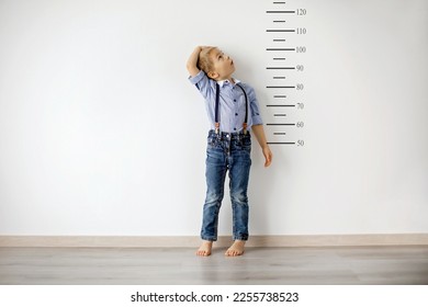 Little child, blond boy, measuring height against wall in room - Shutterstock ID 2255738523