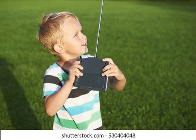 Little child blond boy playing with toy radiocontrolled airplane against green grass lawn background. Holds and operates radio controls