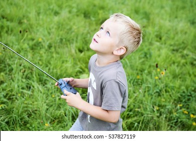 Little child blond boy playing with toy radiocontrolled airplane against green grass lawn background. Holds and operates radio controls - transmitter receiver