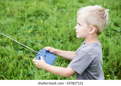 Little child blond boy playing with toy radiocontrolled airplane against green grass lawn background. Holds and operates radio controls - transmitter receiver