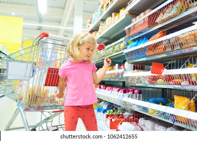 Little Child Blond Girl Shopping in the supermarket, pushing trolley, looking for sweets
