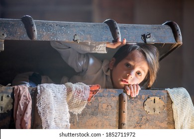 Niño pequeño, niño, escondido en una vieja maleta vintage en el ático, asustado de no ser encontrado