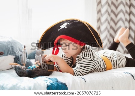 Little child boy in pirate hat and carnival costume playing with pirate ship toy in kid's room. 