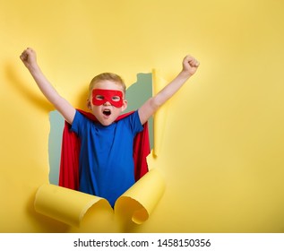 Kleiner Kind, der Superheld spielt und durch gelbe Papierwand bricht. 