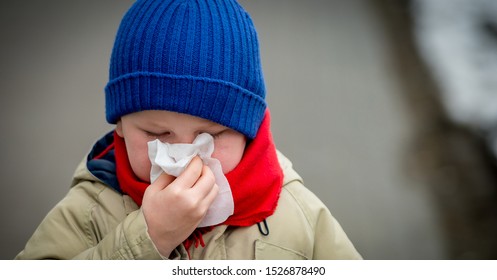 Little Child Boy In Scarf And Hat Blow His Nose. Sick Child With Napkin In Autumn Park. Allergic Kid, Flu Season. Kid With Cold Rhinitis, Get Cold. Back To School