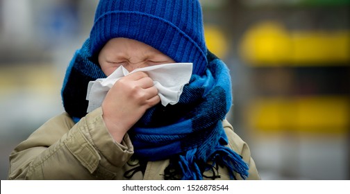 Little Child Boy In Scarf And Hat Blow His Nose. Sick Child With Napkin In Autumn Park. Allergic Kid, Flu Season. Kid With Cold Rhinitis, Get Cold. Back To School