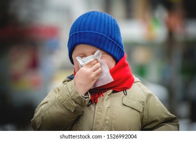 Little Child Boy In Scarf And Hat Blow His Nose. Sick Child With Napkin In Autumn Park. Allergic Kid, Flu Season. Kid With Cold Rhinitis, Get Cold. Back To School