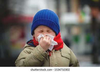 Little Child Boy In Scarf And Hat Blow His Nose. Sick Child With Napkin In Autumn Park. Allergic Kid, Flu Season. Kid With Cold Rhinitis, Get Cold. Back To School