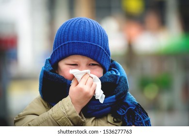 Little Child Boy In Scarf And Hat Blow His Nose. Sick Child With Napkin In Autumn Park. Allergic Kid, Flu Season. Kid With Cold Rhinitis, Get Cold. Back To School