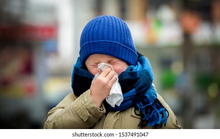 Little Child Boy In Scarf And Hat Blow His Nose. Sick Child With Napkin In Autumn Park. Allergic Kid, Flu Season. Kid With Cold Rhinitis, Get Cold. Back To School