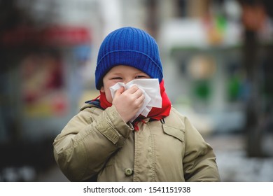 Little Child Boy In Scarf And Hat Blow His Nose. Sick Child With Napkin In Autumn Park. Allergic Kid, Flu Season. Kid With Cold Rhinitis, Get Cold. Back To School