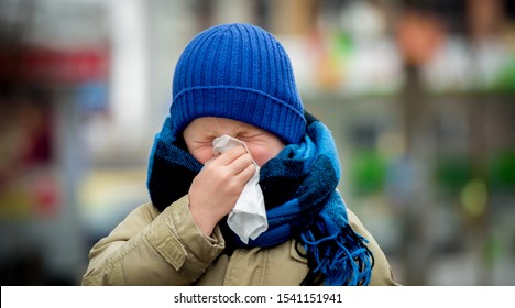 Little Child Boy In Scarf And Hat Blow His Nose. Sick Child With Napkin In Autumn Park. Allergic Kid, Flu Season. Kid With Cold Rhinitis, Get Cold. Back To School