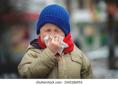 Little Child Boy In Scarf And Hat Blow His Nose. Sick Child With Napkin In Autumn Park. Allergic Kid, Flu Season. Kid With Cold Rhinitis, Get Cold. Back To School