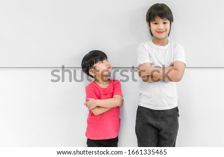 Little child boy standing arms crossed and looking face of tall child at standing arms crossed and smiling. Big and small kid concept at be friends.