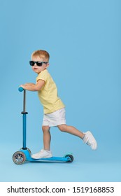 Little Child Boy In Summer Clothes On Scooter Isolated On Blue Wall Background, Children Studio Portrait. People, Childhood Lifestyle Concept. 