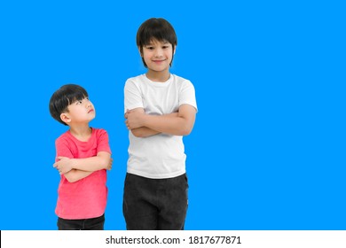 Little child boy in wear red t shirt standing and arms crossed looking for face of tall child at standing arms crossed and smile isolated on blue background. Big and small boy concept with be friends.