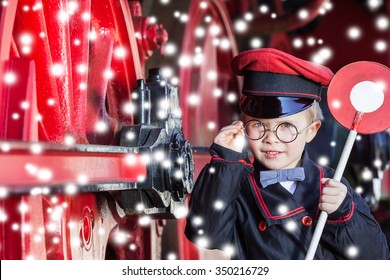 Little Child Boy In Winter As Nostalgic Railroad Conductor Beside Large Wheels Of A Steam Locomotive With Snowflakes And Copy Space/Smiling Train Conductor Boy In Winter 