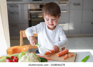 Little Child Cut Fresh Carrot With Knife Alone.kid Helper Cook Vegetable In Kitchen Home.young Boy Training Skill Montessori And Learning Concept. Mixed Race Asian-German Learn Cooking.