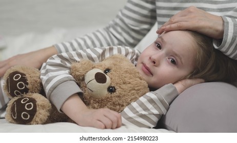 little child daughter lies her mother lap hugging teddy bear. time sleep kid. mom strokes cares girl daughter head. nice relaxation before bed. childhood dream arm mother. happy family life together