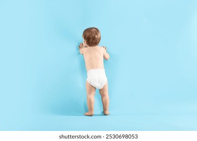 Little child in diaper on light blue background, back view