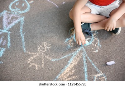 Little Child Drawing Family With Chalk On Asphalt