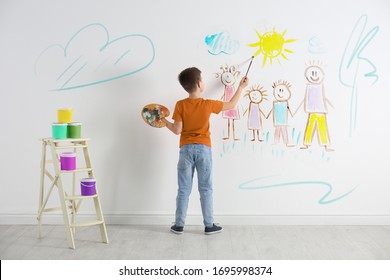 Little Child Drawing Family On White Wall Indoors