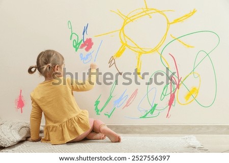 Little child drawing on white wall, back view