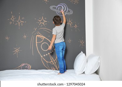 Little child drawing rocket and chalk wall in bedroom