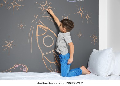 Little Child Drawing Rocket With Chalk On Wall In Bedroom