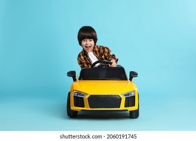 Niño pequeño conduciendo coche de juguete amarillo sobre fondo azul claro