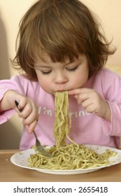 Little Child Eating Pasta With Pesto Sauce