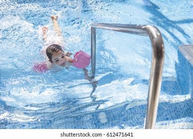 Little child enjoying swimming pool indoors. Cute toddler girl wearing armbands having fun in the water