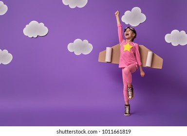 Little child girl in an astronaut costume is playing and dreaming of becoming a spaceman. Portrait of funny kid on a background of ultraviolet wall with white clouds.