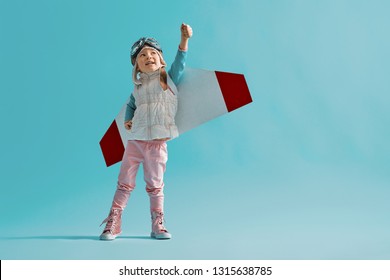 Little child girl in an astronaut costume is playing and dreaming of becoming a spaceman. Portrait of funny kid on a background of bright blue wall.