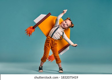 Little Child Girl In An Astronaut Costume Is Playing And Dreaming Of Becoming A Spaceman. Isolated Blue Background. Copy Space