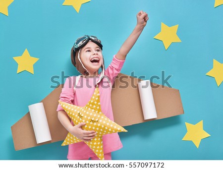 Little child girl in an astronaut costume is playing and dreaming of becoming a spaceman. Portrait of funny kid on a background of bright blue wall with yellow stars.