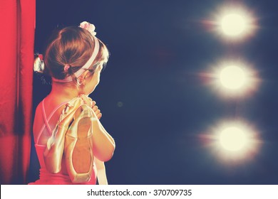 Little Child Girl Ballerina Ballet Dancer On The Stage In Red Side Scenes And Looking In Odeum