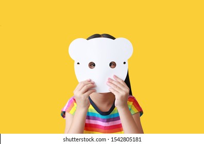 Little Child Girl Holding Blank White Animal Paper Mask Fronting Her Face Isolated On Yellow Background. Idea And Concept For Kid Dressed Up Playing Animal Face.