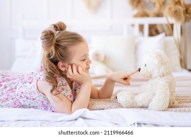 a little child girl at home in a calm natural interior in beige color plays and cuddles with a soft teddy bear - Powered by Shutterstock