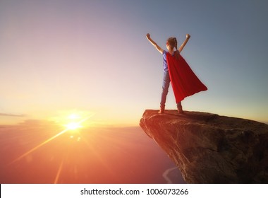 Little child girl is playing superhero. Child on the background of sunset sky. Girl power concept