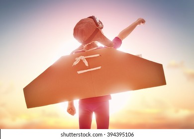 Little child girl plays astronaut. Child on the background of sunset sky. Child in an astronaut costume plays and dreams of becoming a spaceman. - Shutterstock ID 394395106