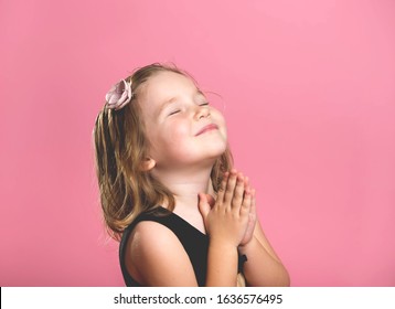 Little Child Girl Praying. Kid With Hands Folded In Prayer. Child Face Looking And Asking Isolated On Pink