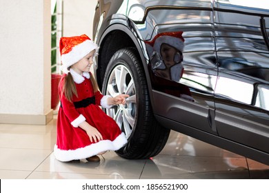 Little Child Girl In Red Santa Suit Stands With Her Back And Looks At The New Car