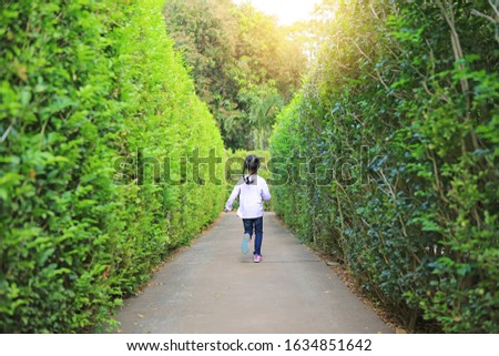 Little child girl running forward into garden Maze. Kid playing in labyrinth for fun and entertainment. Back view.