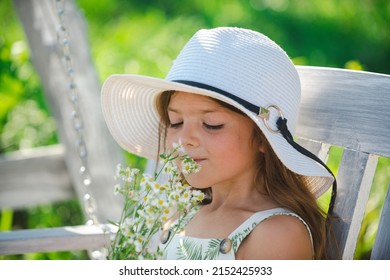Little Child Girl Is Smelling Flowers On Green Backyard. Adorable Kid On A Summer Meadow And Smelling Flowers. Summer Fun For Family With Kids Outdoors In A Beautiful Spring Garden.