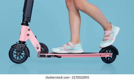 Little Child Girl In Summer Clothes On Scooter Isolated On Blue Wall Background, Children Studio Portrait. People, Childhood Lifestyle Concept.