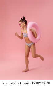 Little Child Girl In Swimwear With Inflatable Rubber Ring Running On Pink Background